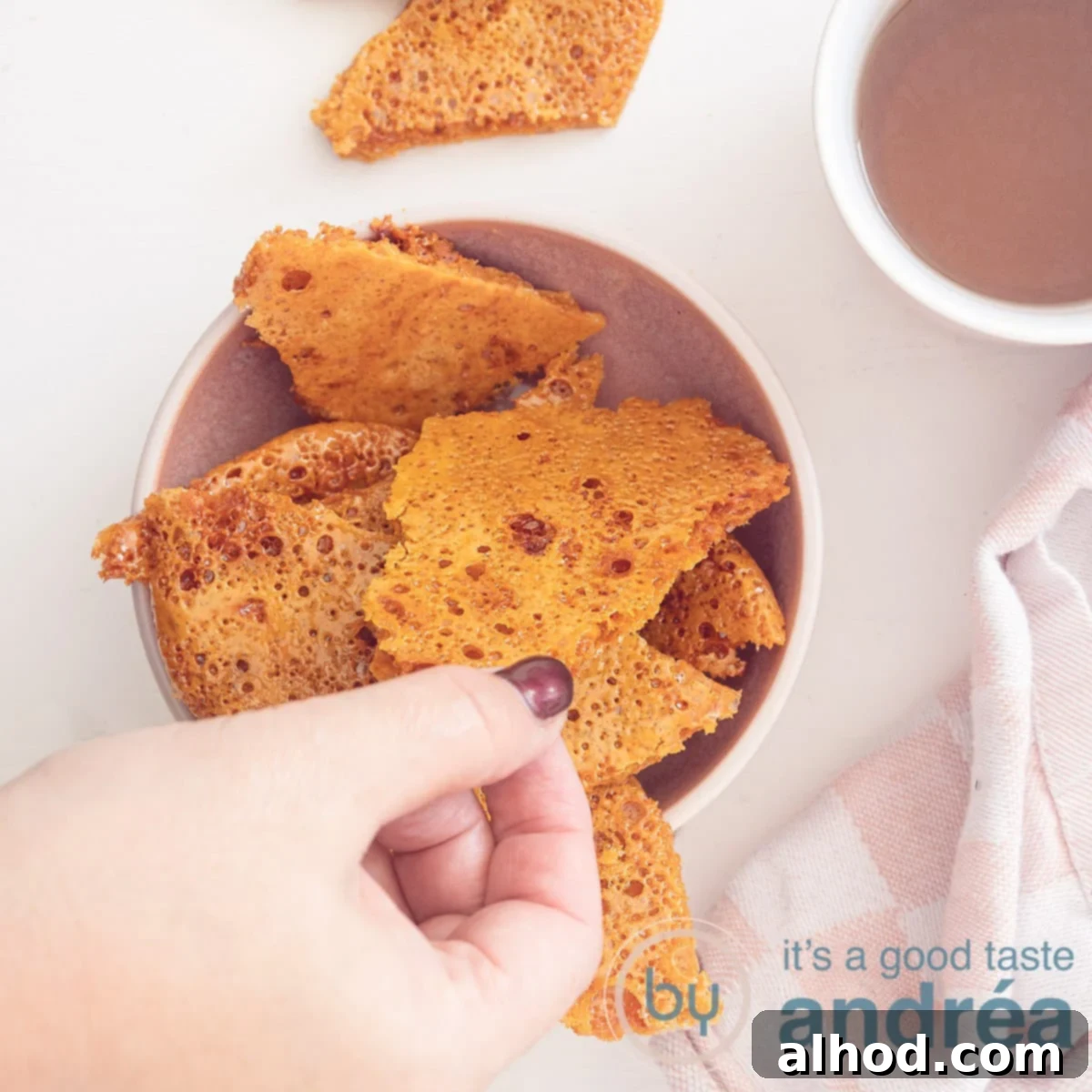 A square photo with a pink tray with honeycomb pieces in the middle. A hand grabs a piece. Top right a mug with tea.