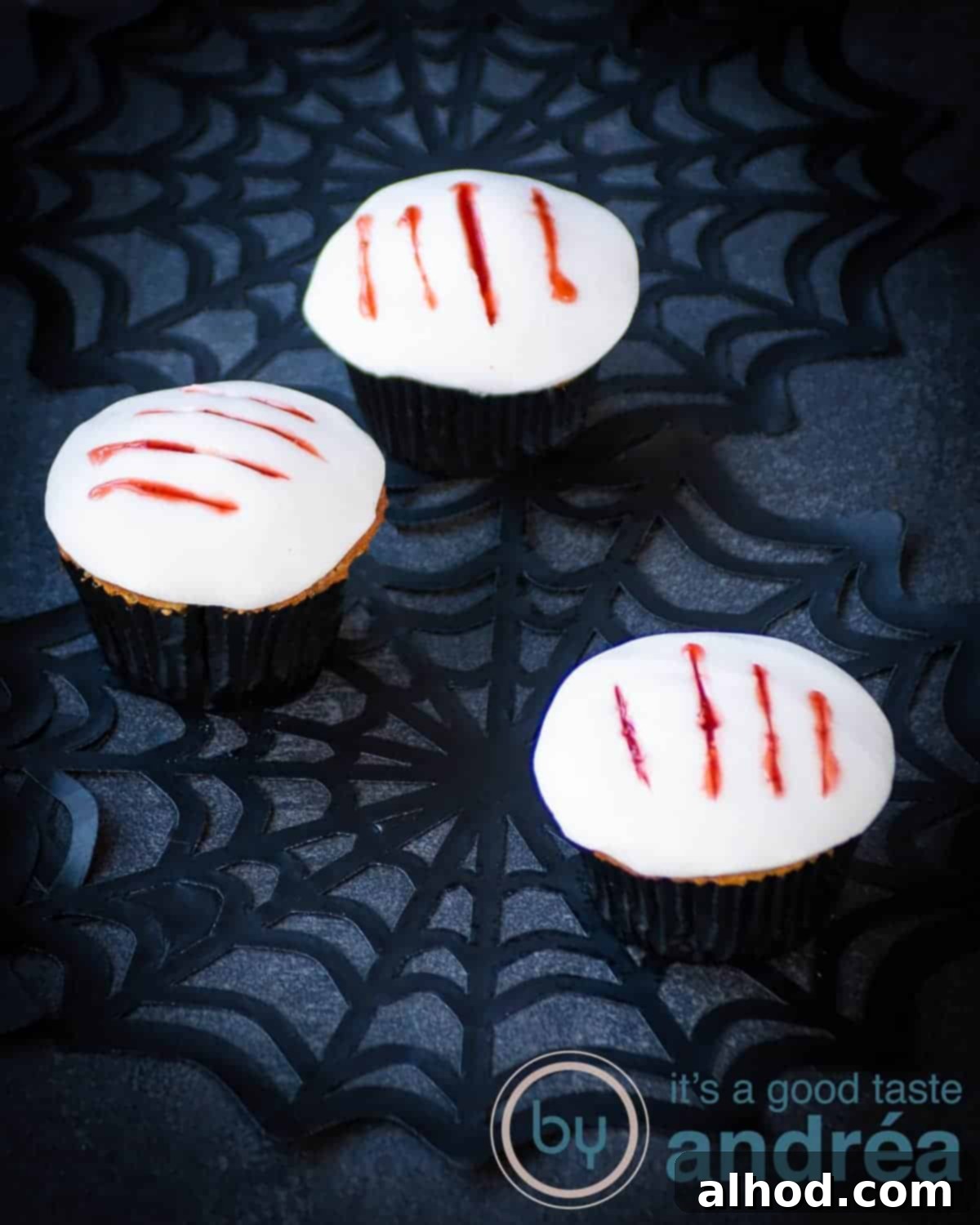 Howling Werewolf Claw Cupcakes 2 Three Werewolf Claw Cupcakes on a dark surface with cobwebs, featuring white fondant tops with jagged claw marks revealing red strawberry 'blood' beneath.