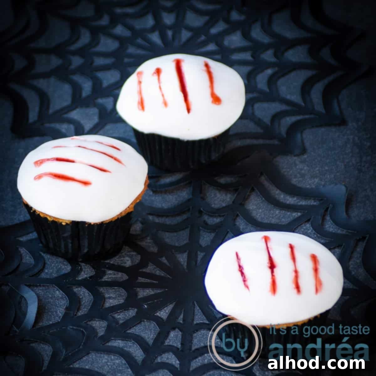 Howling Werewolf Claw Cupcakes 4 A square photo with three cupcakes with a white fondant layer, with blood streaks of jam on top, set against a spooky backdrop.