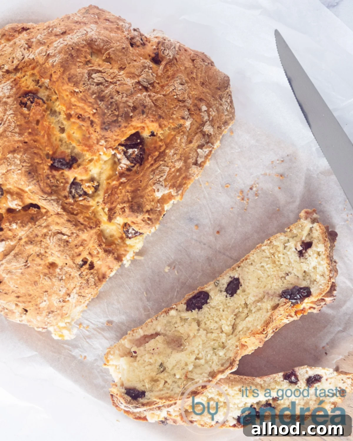A photo from above of a white background, on top of which is a soda bread. Two slices cut off are in front of it. A knife on the right.