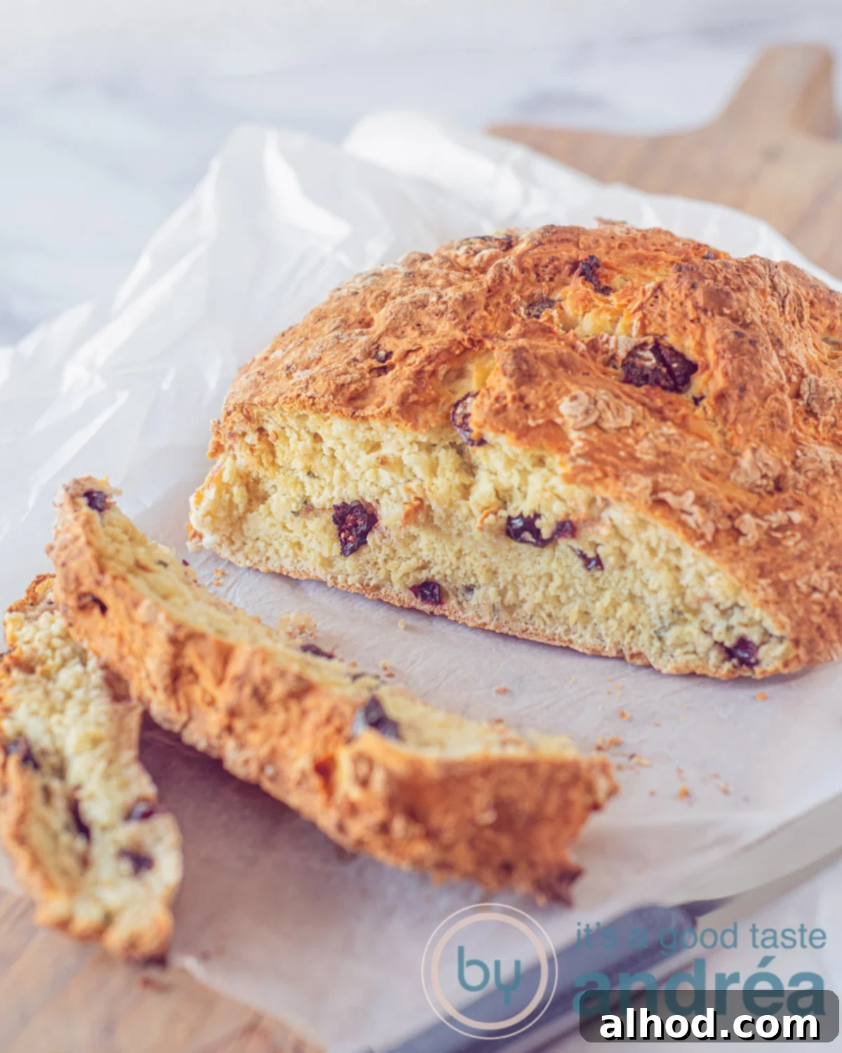 Simple Irish Soda Bread 5 Soda Bread with cranberries and roseamary on a white baking paper on a wooden board. Two slices cut of.