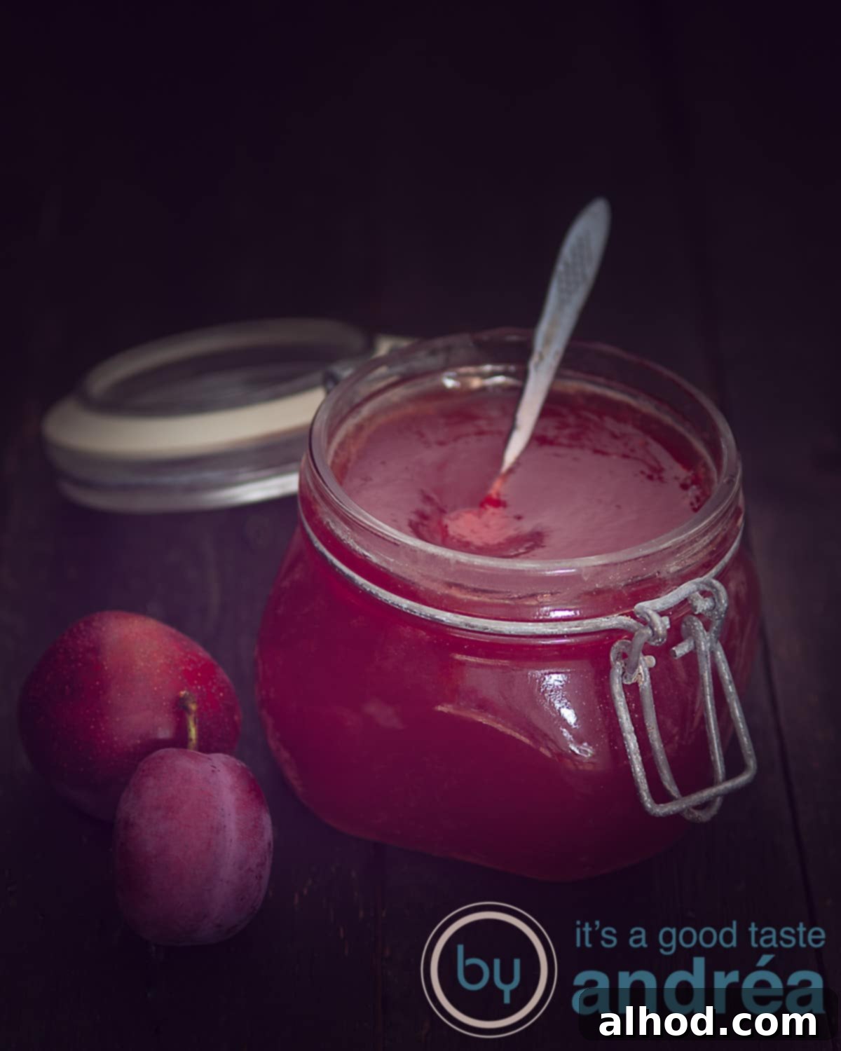 Luscious Plum Vanilla Delight 2 A beautifully presented jar of homemade plum jam with vanilla, set against a rustic dark background. Two fresh plums are artfully placed to the left of the jar, highlighting the main ingredient.