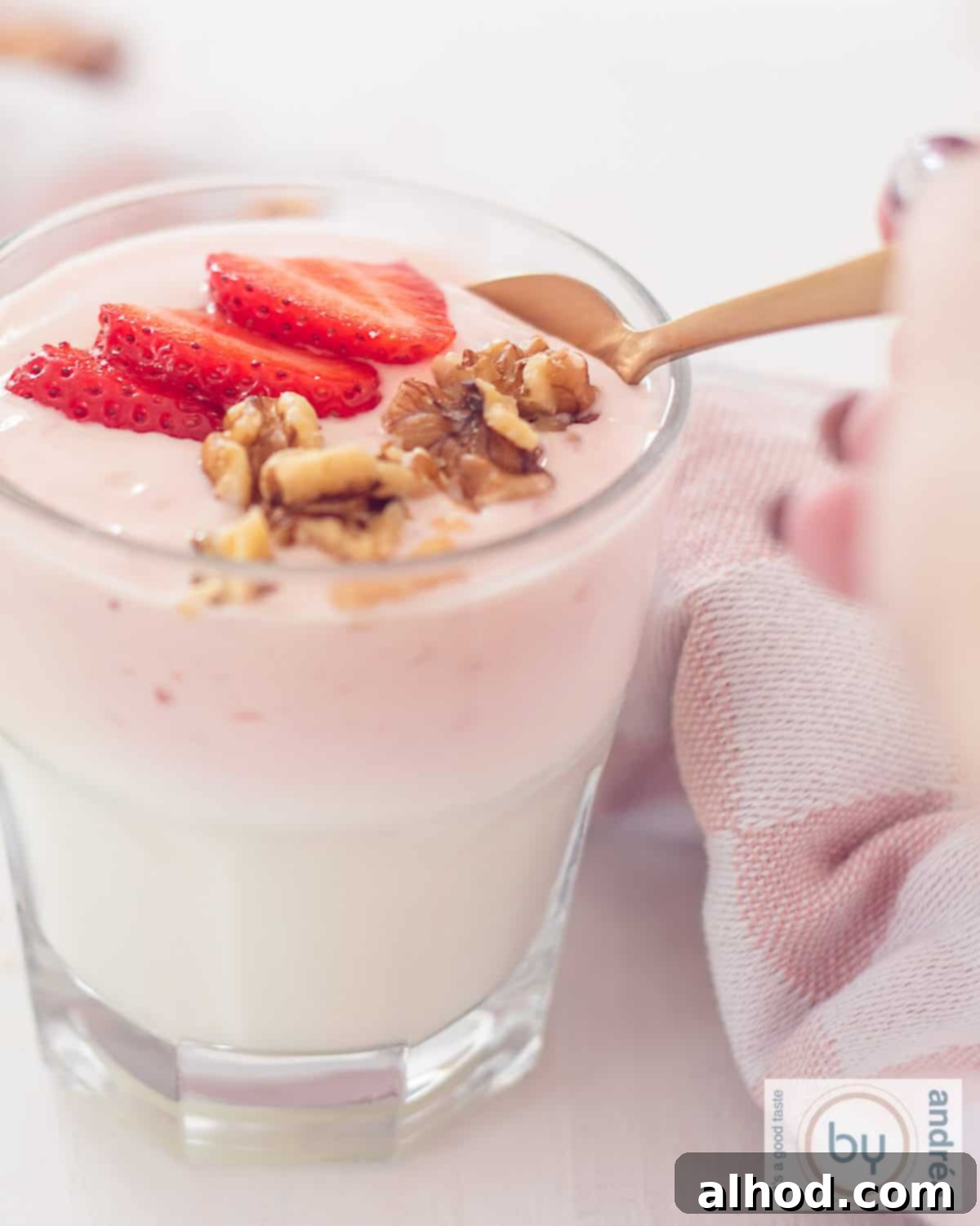 Effortless Strawberry Yogurt Parfait 2 A glass filled with homemade strawberry yogurt, fresh strawberries and walnuts. A golden spoon takes a scoop.