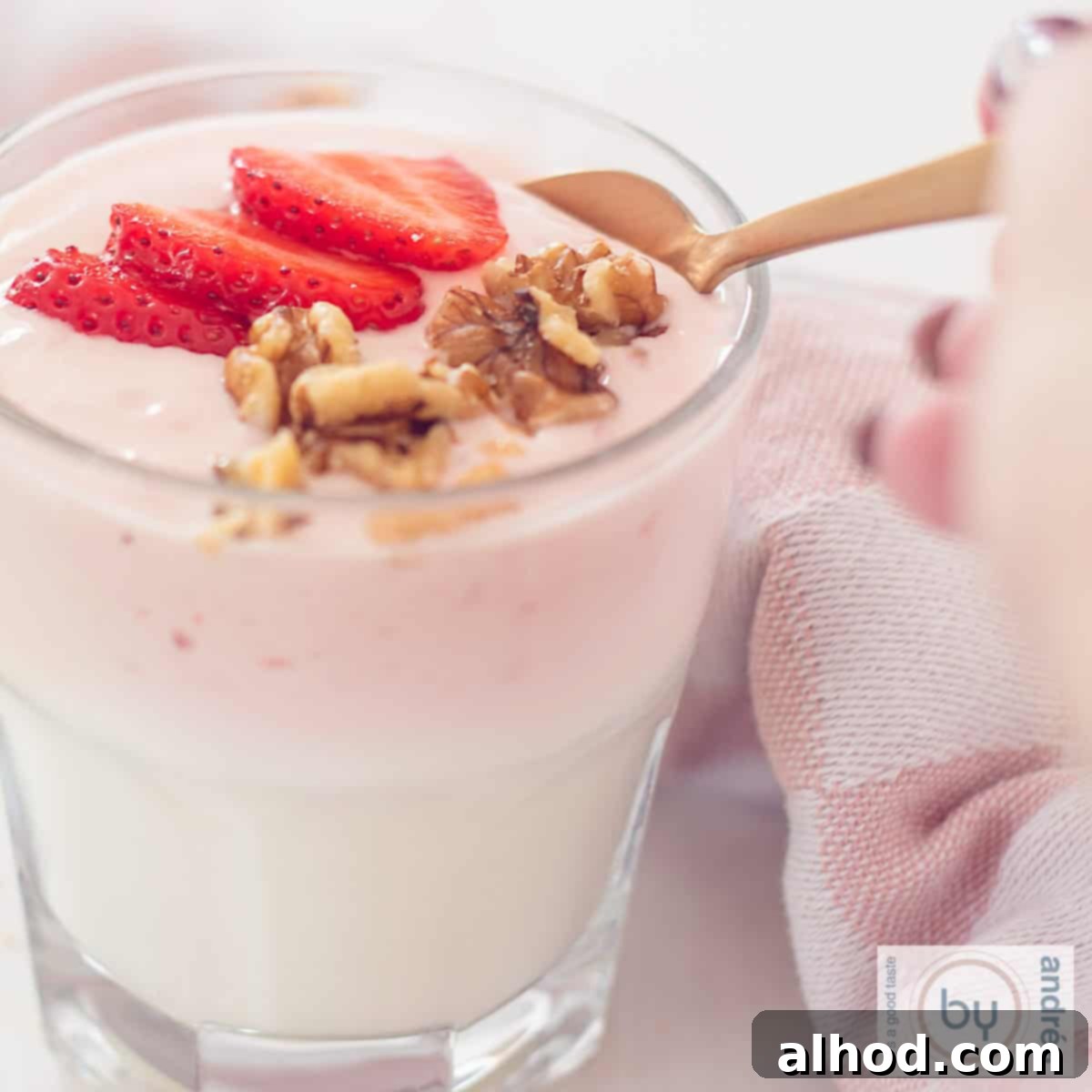 Effortless Strawberry Yogurt Parfait 4 A square photo of a glass filled with homemade strawberry yogurt, walnuts and fresh strawberries. A golden spoon takes a scoop.