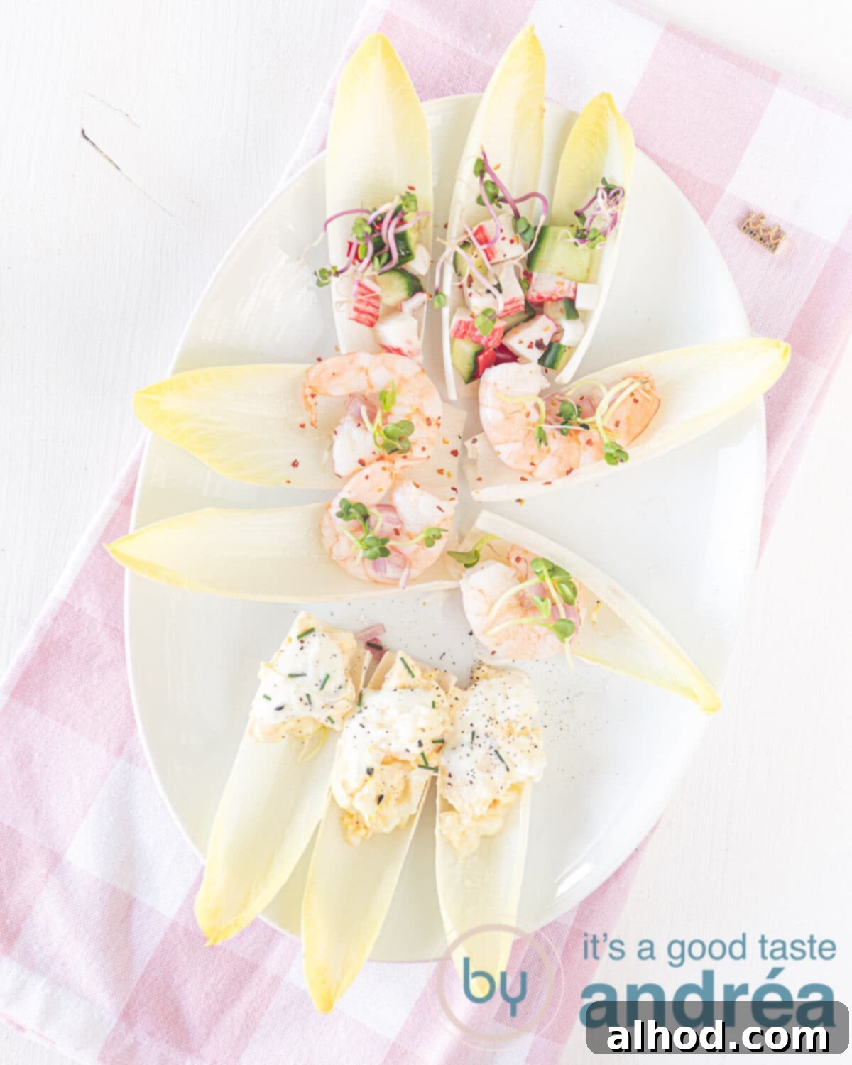 A white plate with chicory boats filled with crab, shrimp and egg salad, artfully arranged for a party appetizer.