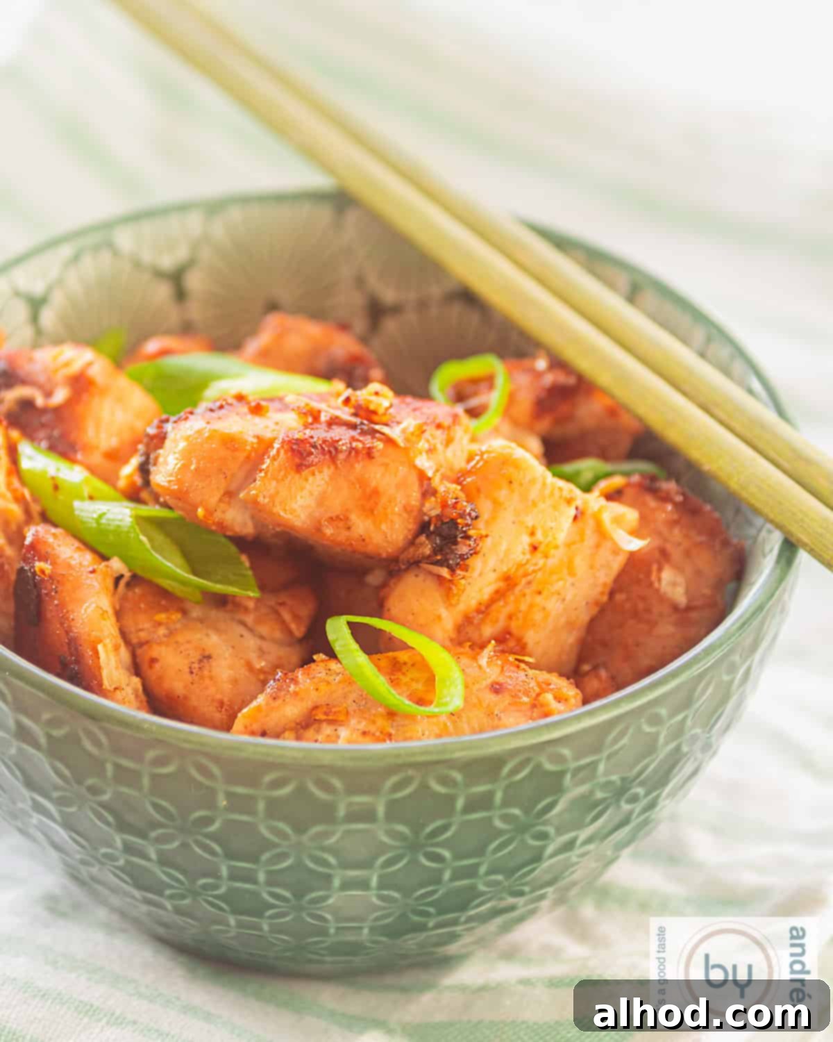Whip Up Thai Chicken in 15 Minutes 2 A height shot of a green bowl filled with chicken made with four sauces and spring onions. Two chopsticks are placed on top.