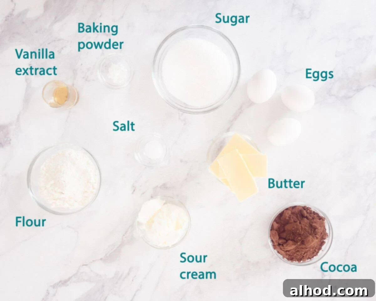 Decadent Triple Chocolate Cupcakes 3 A curated display of all the dry and wet ingredients needed for Triple Chocolate Cupcakes, including flour, cocoa powder, butter, sugar, eggs, vanilla extract, and sour cream, on a white background.
