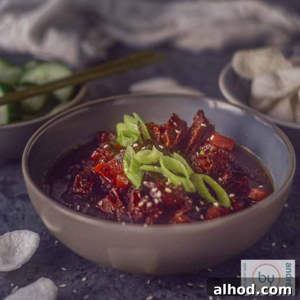Easy Crockpot Mongolian Beef 6 A square picture with a grey bowl filled with slow cooker mongolian beef with spring onion garnish and some prawn crackers.