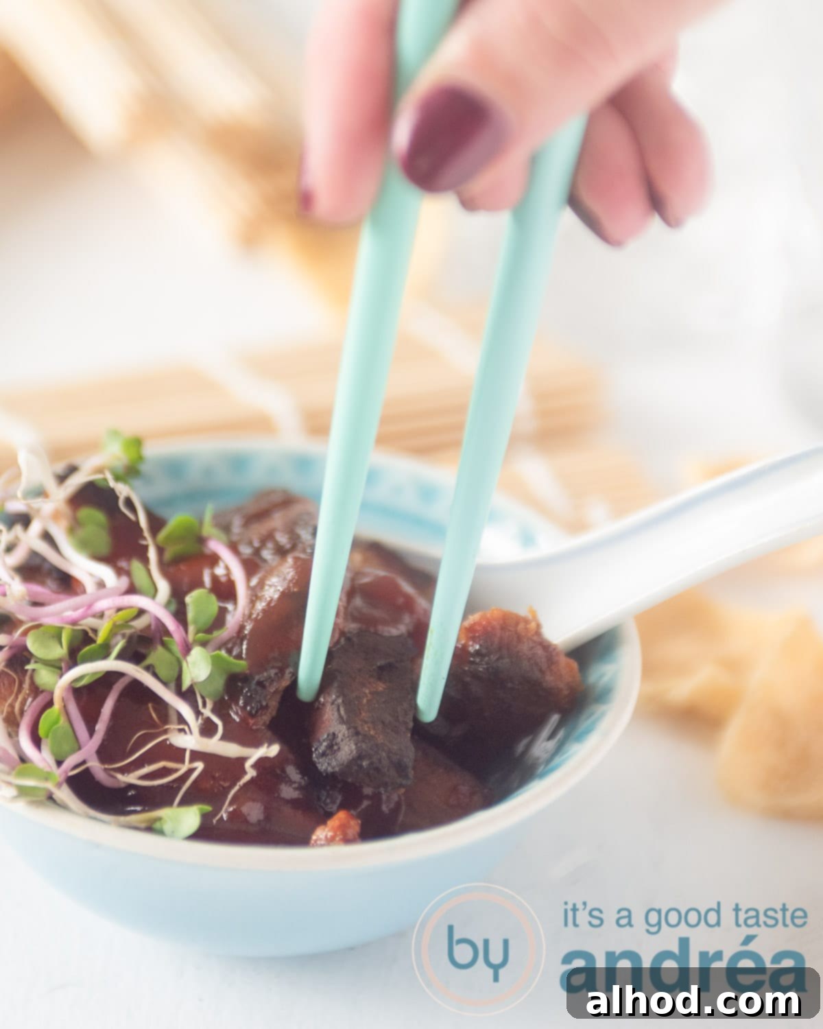 Authentic Chinese Babi Pangang Recipe 2 A hand taking out a piece of crispy Babi Pangang out of a blue bowl, highlighting the glossy sweet sauce.