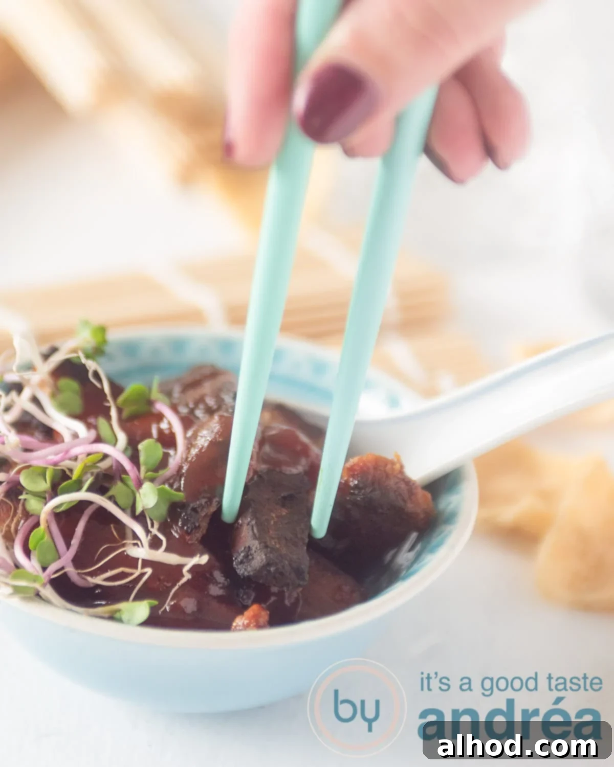 Authentic Chinese Babi Pangang Recipe 2 A hand taking out a crispy piece of Babi Pangang pork from a vibrant blue bowl, glistening with sweet and sour sauce.