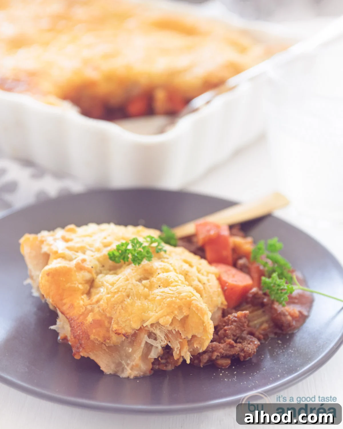 Puff Pastry Beef Pot Pie 2 Hearty Beef Shepherd's Pie with a golden, flaky puff pastry crust, beautifully browned and served on a grey plate. A white casserole dish with more pie sits in the background, promising endless comfort.