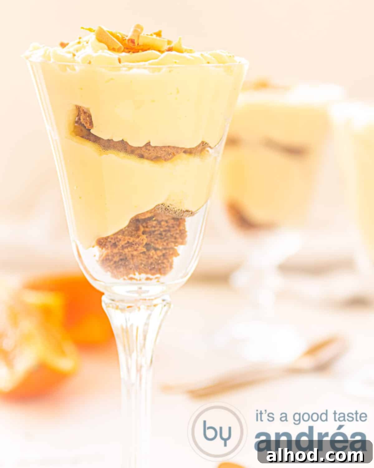 Zesty Orange Delight 2 A glass filled with orange custard and bastogne cake. A golden spoon and oranges on a white surface.