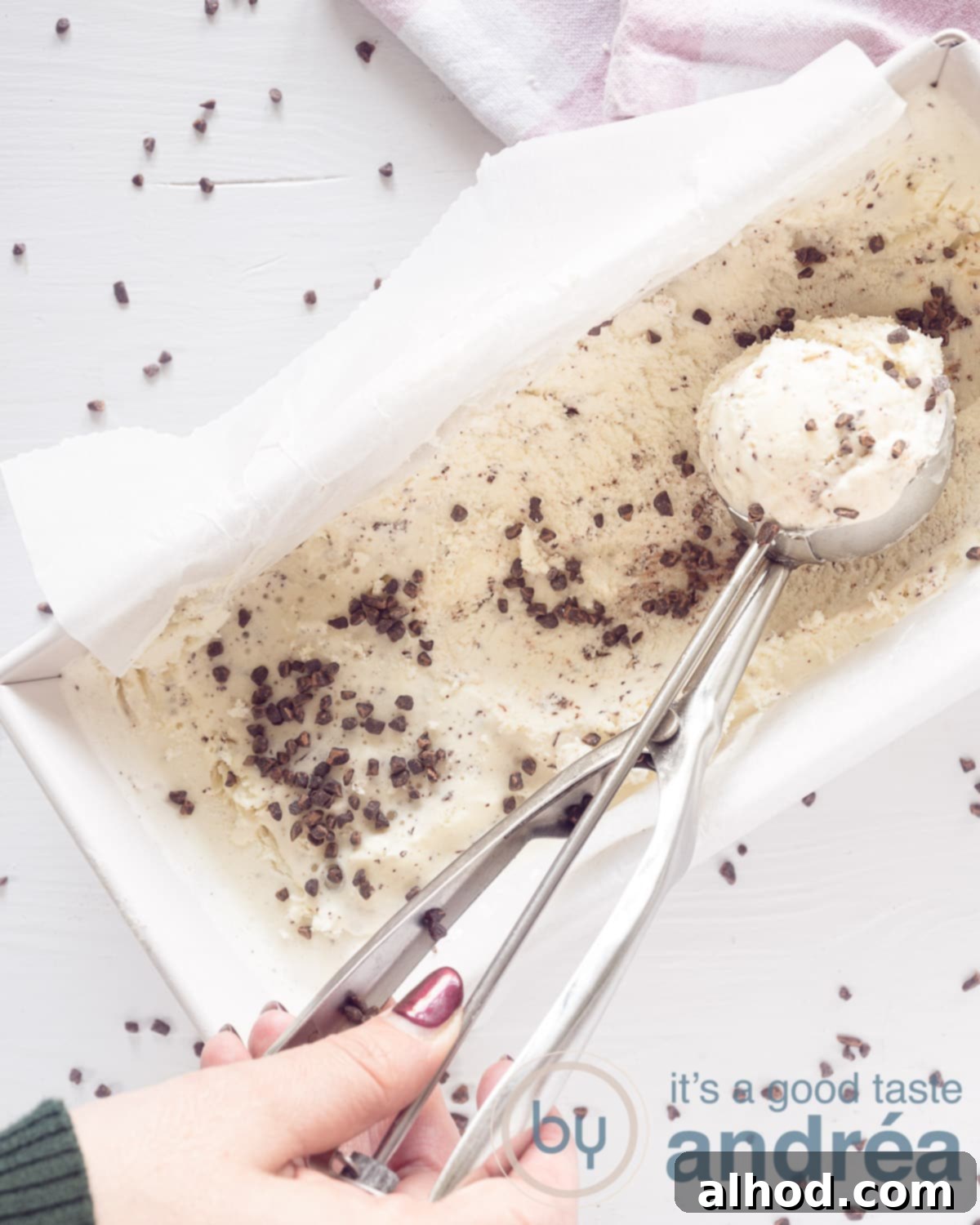 Dreamy No-Churn Honey Chocolate Ice Cream 2 A top-down view of creamy chocolate honey ice cream in a cake tin, with one scoop already taken. The background is white with scattered chocolate shavings.