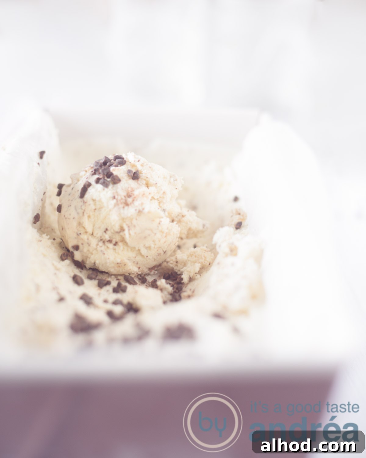 Dreamy No-Churn Honey Chocolate Ice Cream 5 A pink cake tin filled with creamy honey ice cream and visible dark chocolate chunks, with an ice cream scoop on top. The background is white.