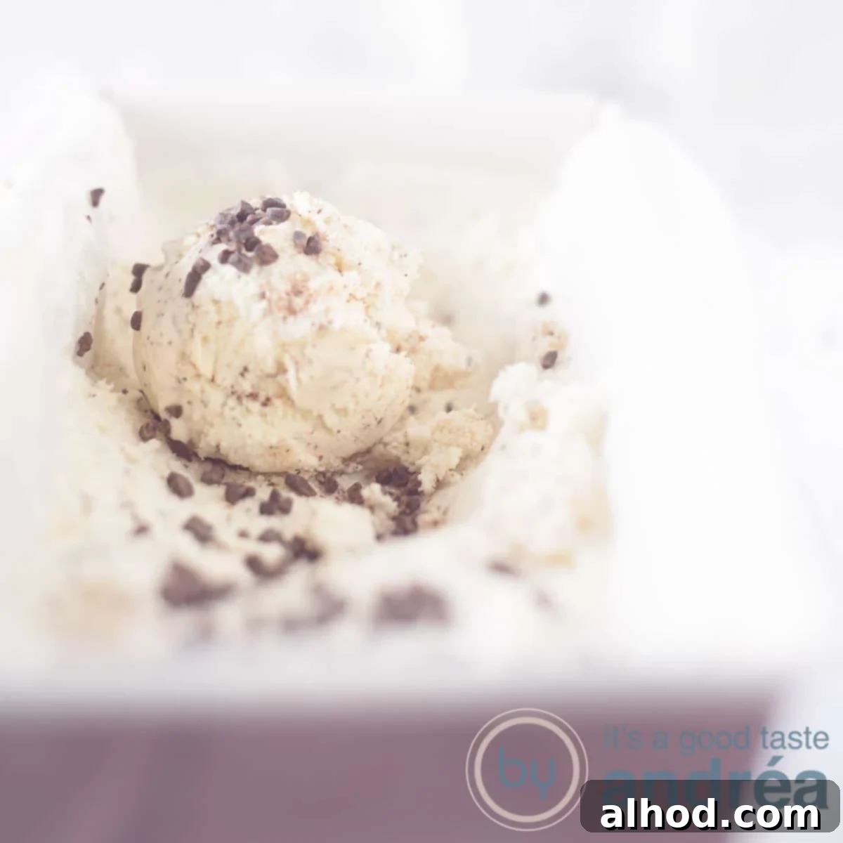 Dreamy No-Churn Honey Chocolate Ice Cream 6 A square photo of a pink cake tin with chocolate honey ice cream. A scoop of ice cream on top.