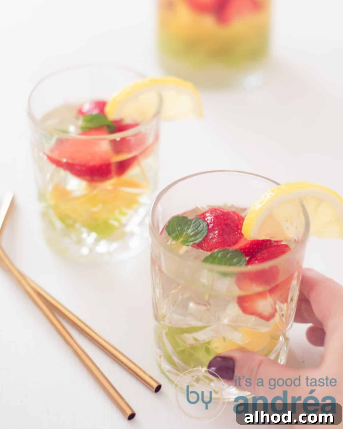 Crafting the Perfect Clerico Punch 2 Two glasses filled with Clerico, a white sangria, adorned with fresh fruit and gold straws, on a pristine white background. A hand reaches for one of the glasses, inviting a refreshing sip.