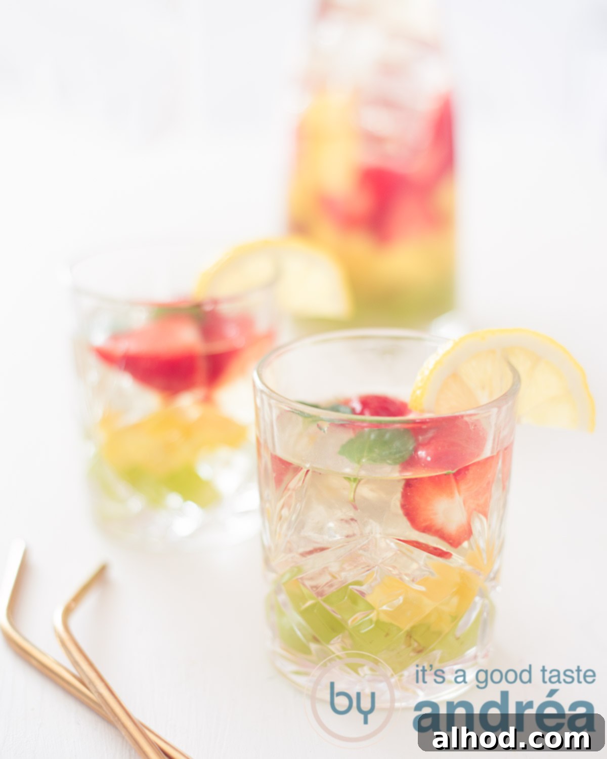 Crafting the Perfect Clerico Punch 5 Two beautiful glasses of Clerico, the white sangria, garnished with grapes, mango, and strawberries. In the background, a large pitcher filled with more Clerico sits on a pristine white surface, inviting enjoyment.