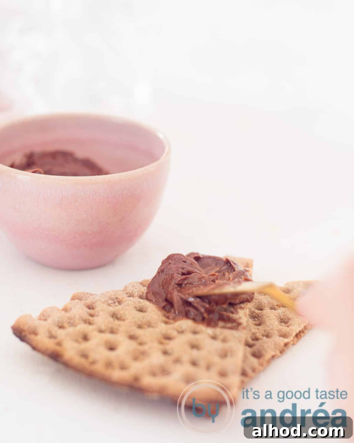 Decadent Chocolate Butter Spread 5 A person is smearing with a knife chocolate butter on toast. A pink bowl of chocolate butter is in the background.