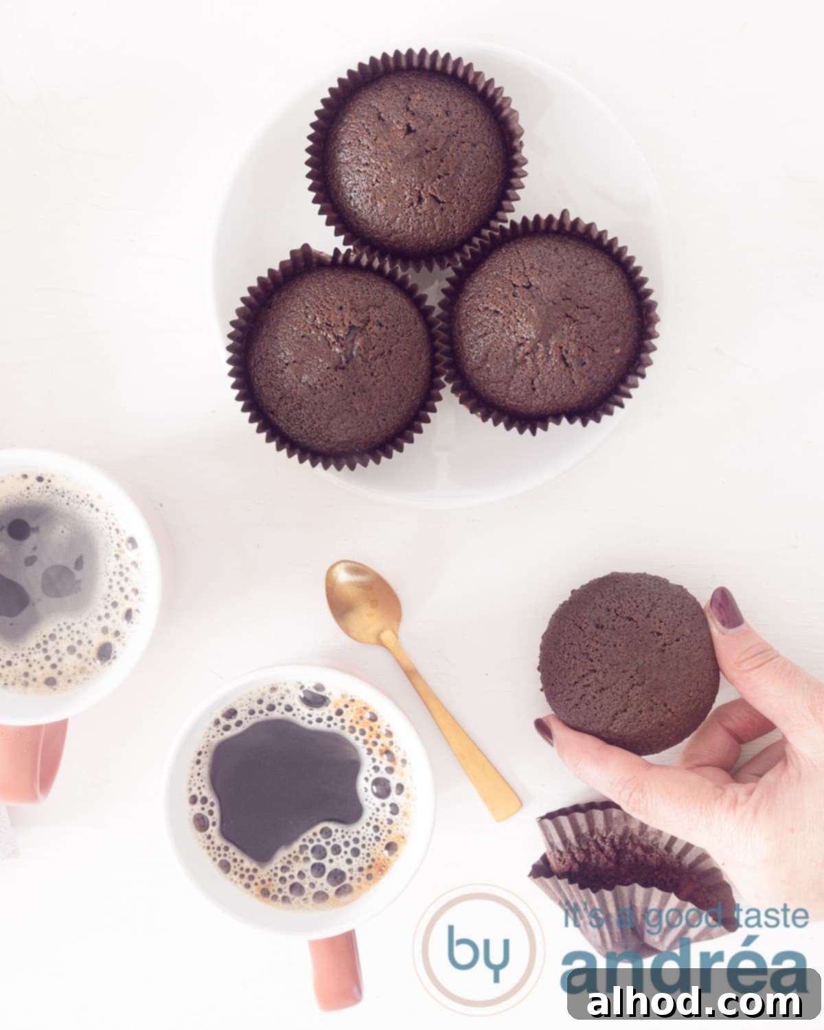 Vegan Chocolate Cupcakes 2 A photo from above of a chocolate cupcake, milk free, bottom right. Two cups of coffee at the bottom left. At the top a white plate with three cupcakes.