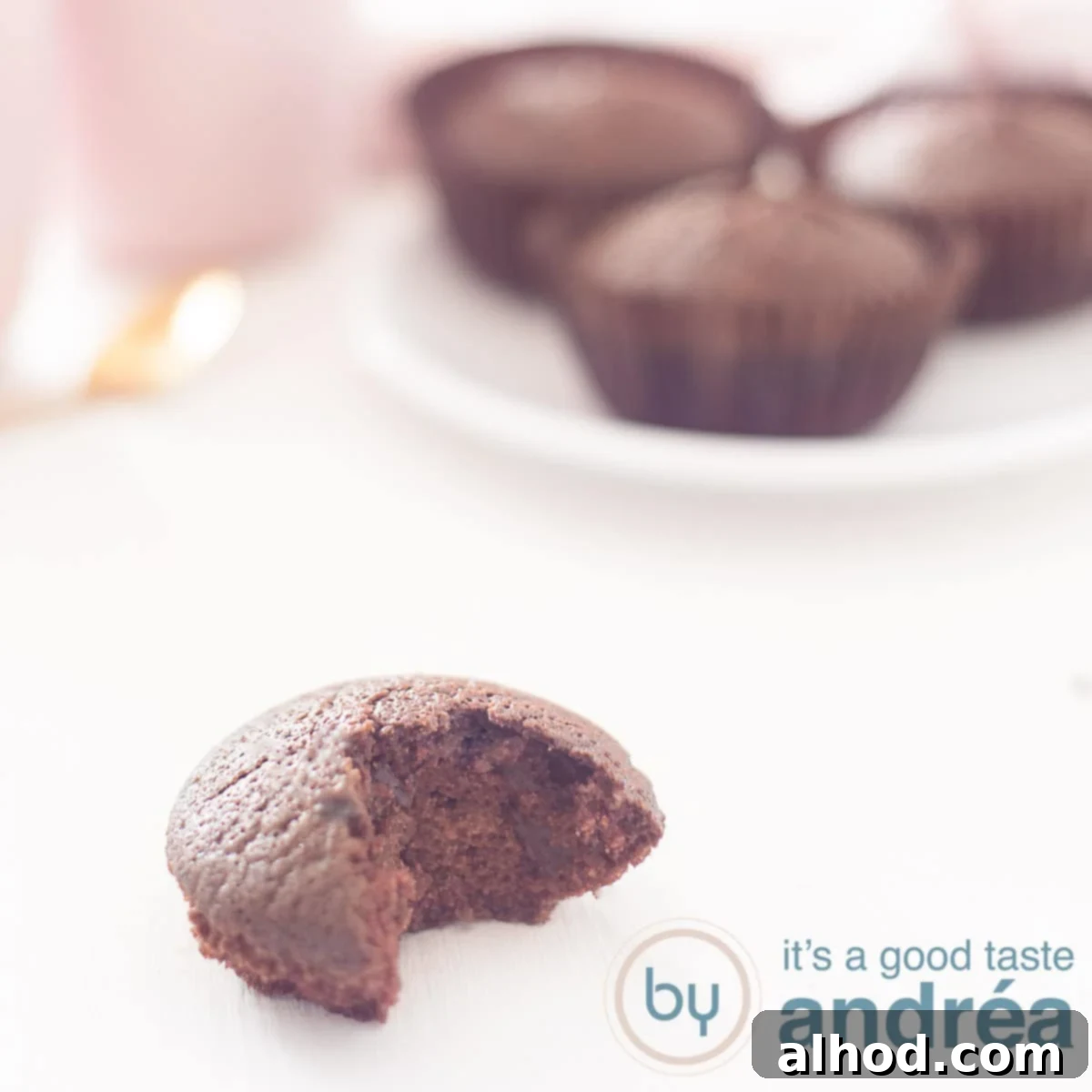 A square photo with a cupcake with chocolate in the front with a bite out. In the background another plate with lactose-free cupcakes.