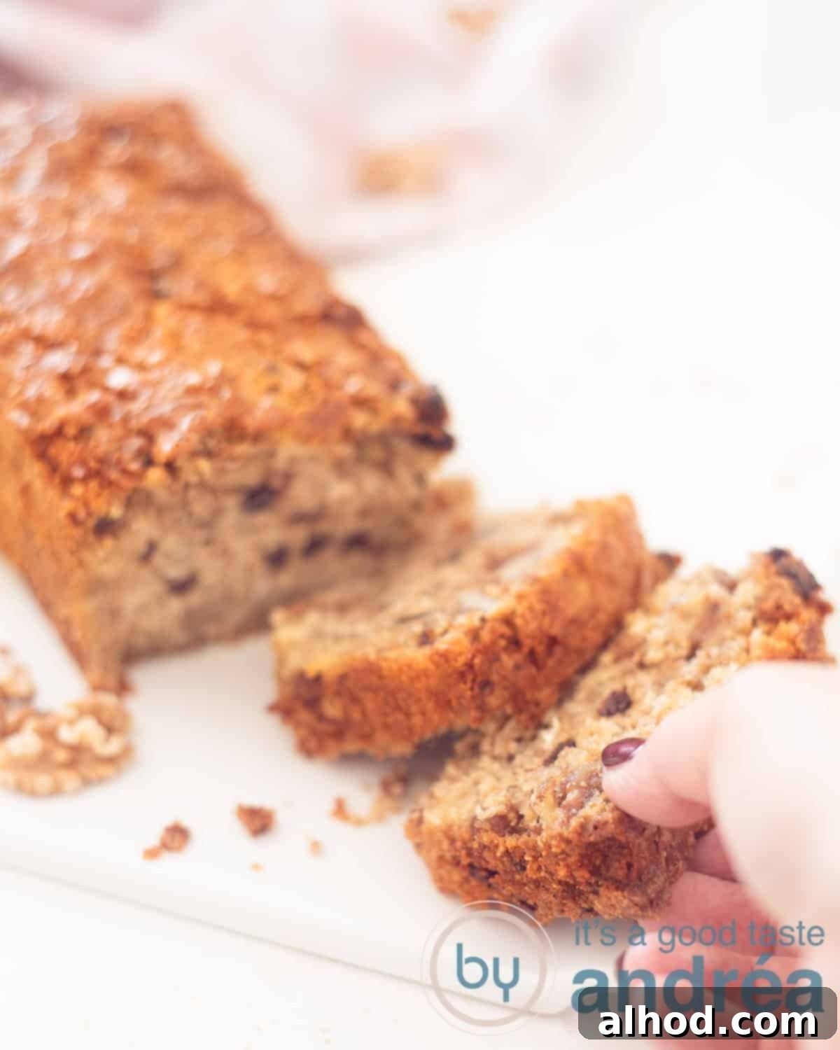 Granola Cake Delight 5 An elevation photo with a granola cake on a white background, where 2 slices have been cut off. A hand grabs the front slice