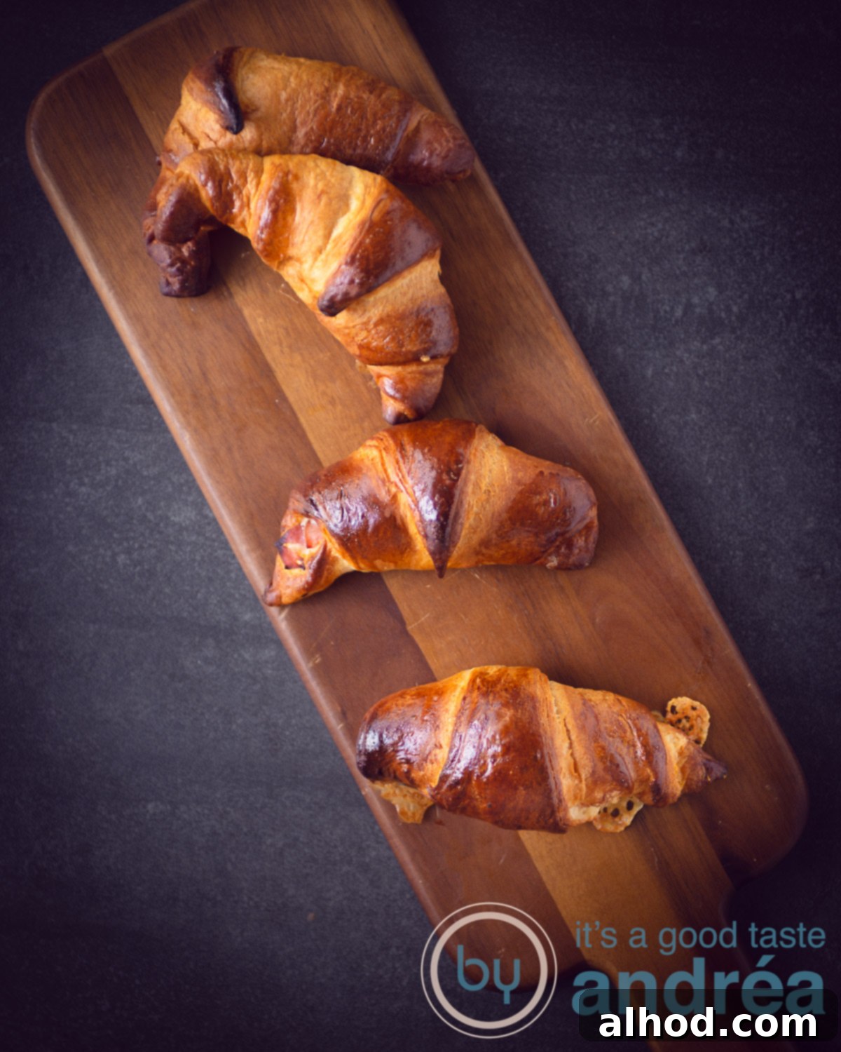 Flaky Ham and Cheese Puff Pastry Croissants 5 four Ham cheese croissants on a wooden plate on a dark grey background, showcasing their golden perfection.