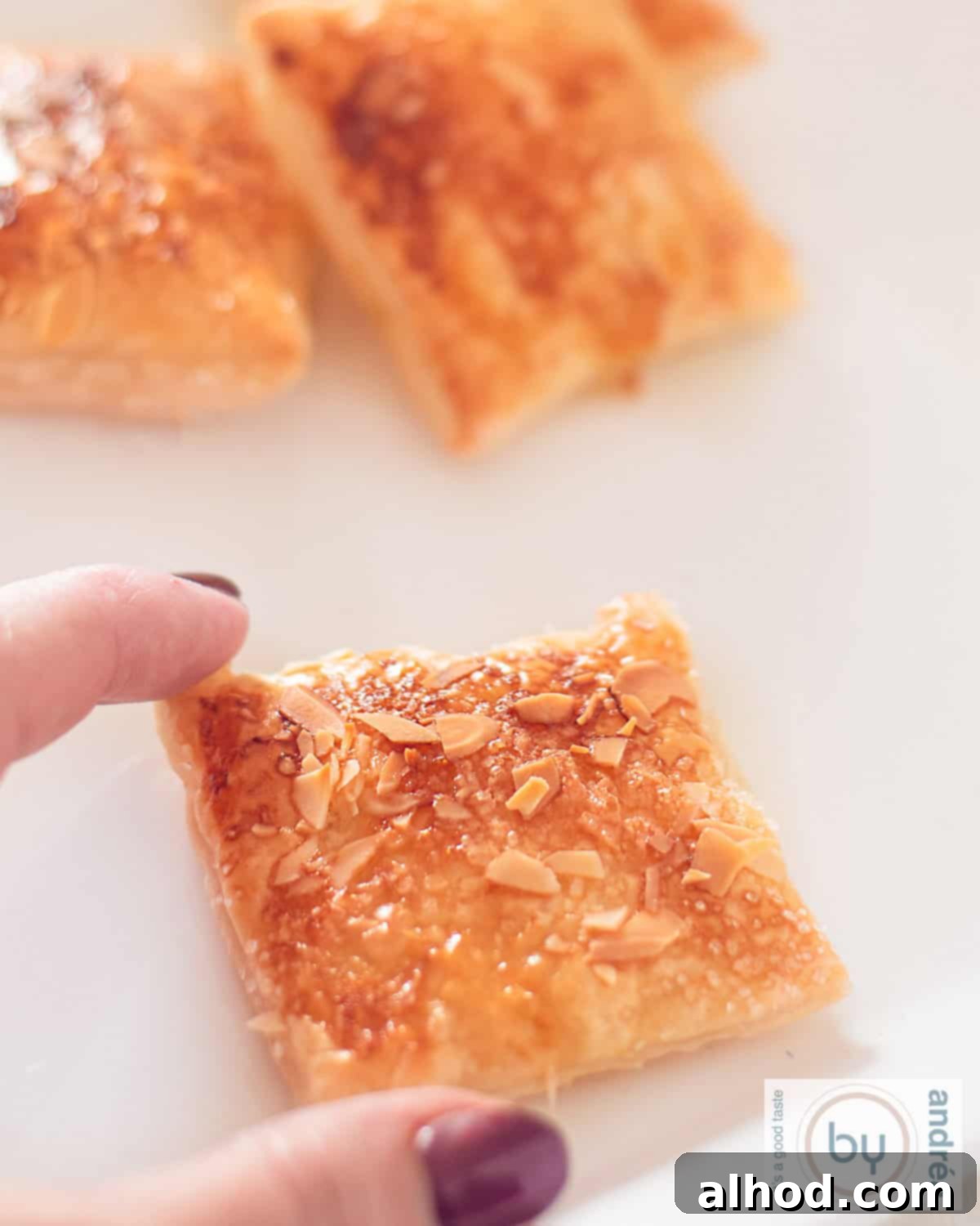 Flaky Zesty Lemon Puff Pastry Cookies 3 A hand holding a perfectly baked lemon puff pastry cookie with toasted almonds, showing its golden color and delicate layers.