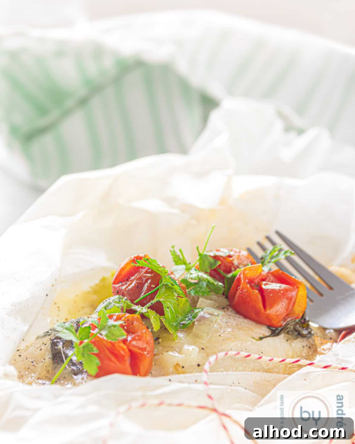 Cod en Papillote 2 Cod fish package from the oven in white baking paper. A green white towel in the back