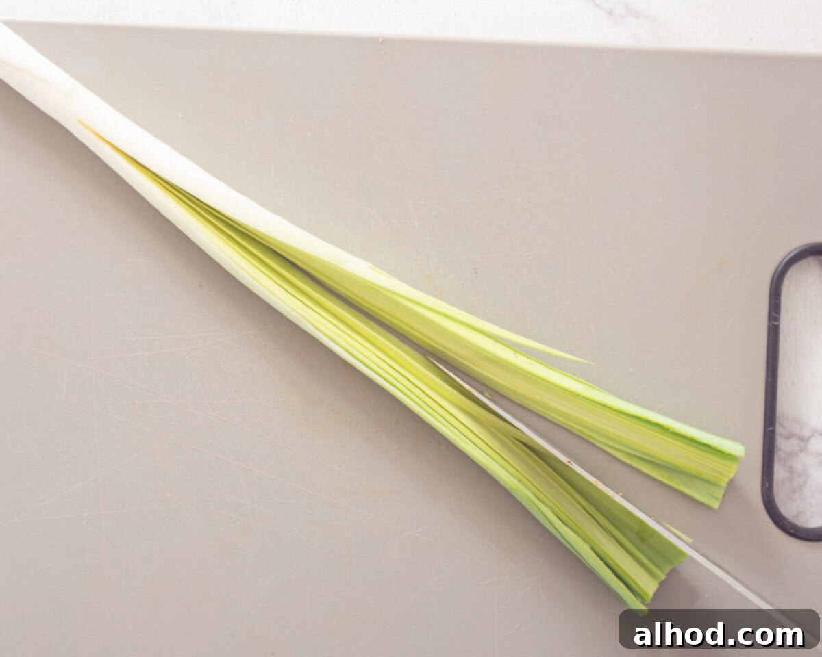 Speedy Leek Cleaning Made Simple 4 A chef's knife making a precise lengthwise cut into a leek, starting from just above the root and extending towards the top, with the root remaining intact.