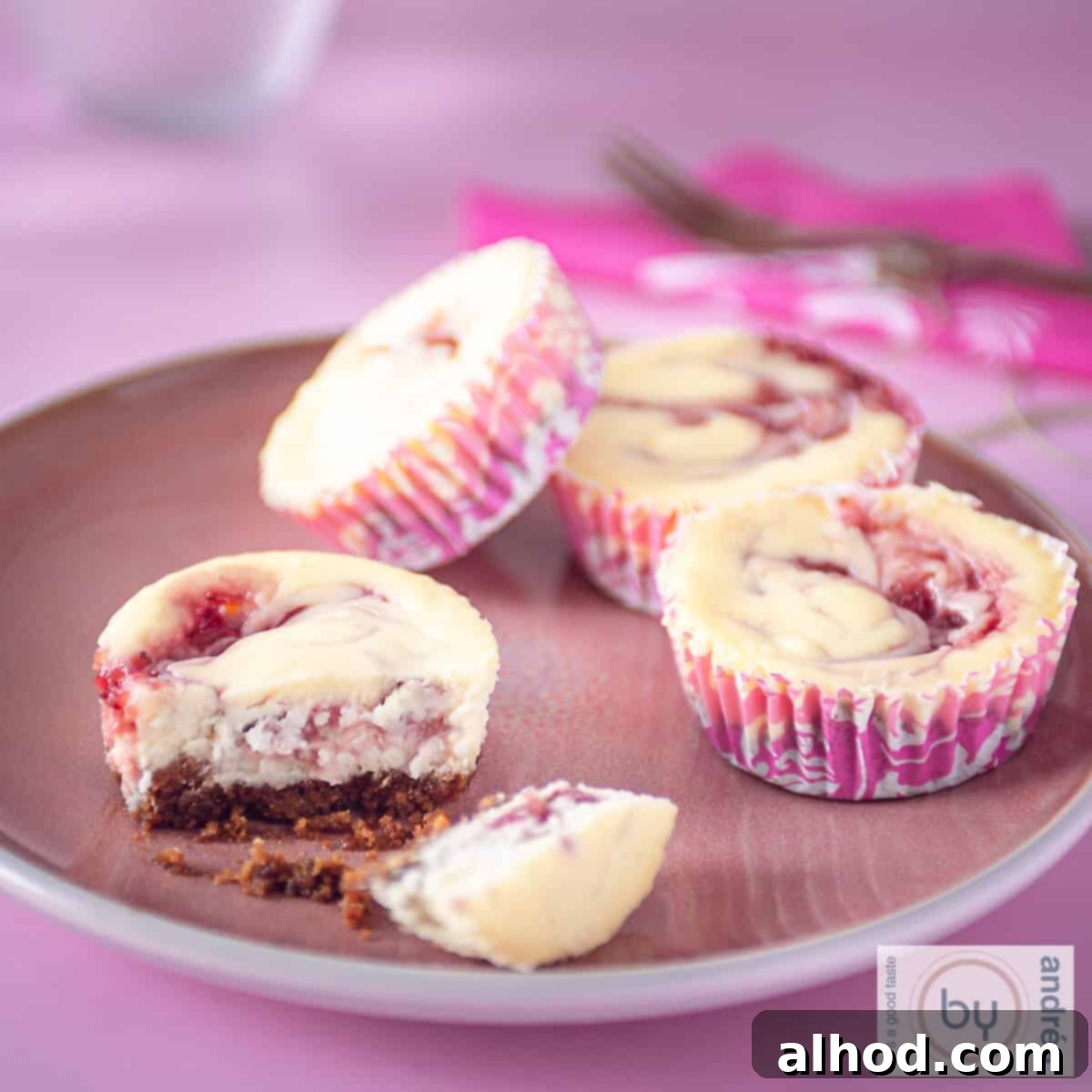 Decadent Strawberry Swirl Cheesecake Minis 4 A square photo with a pink plate with pink cupcakes, four of which 1 is broken in half and you can clearly see the bottom.