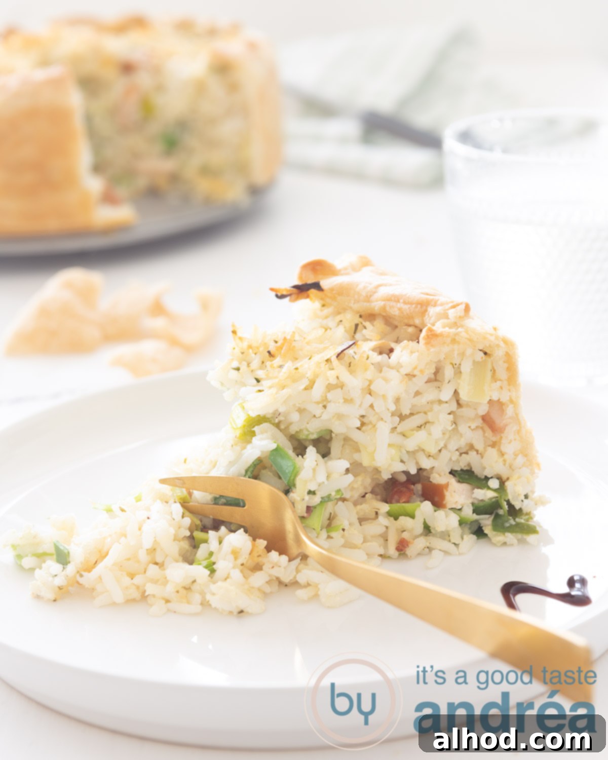 Golden Chicken Leek Rice Quiche 4 Leek rice quiche with smoked chicken piece on a white plate. A golden fork is taking a bite. In the background the remaining quiche.