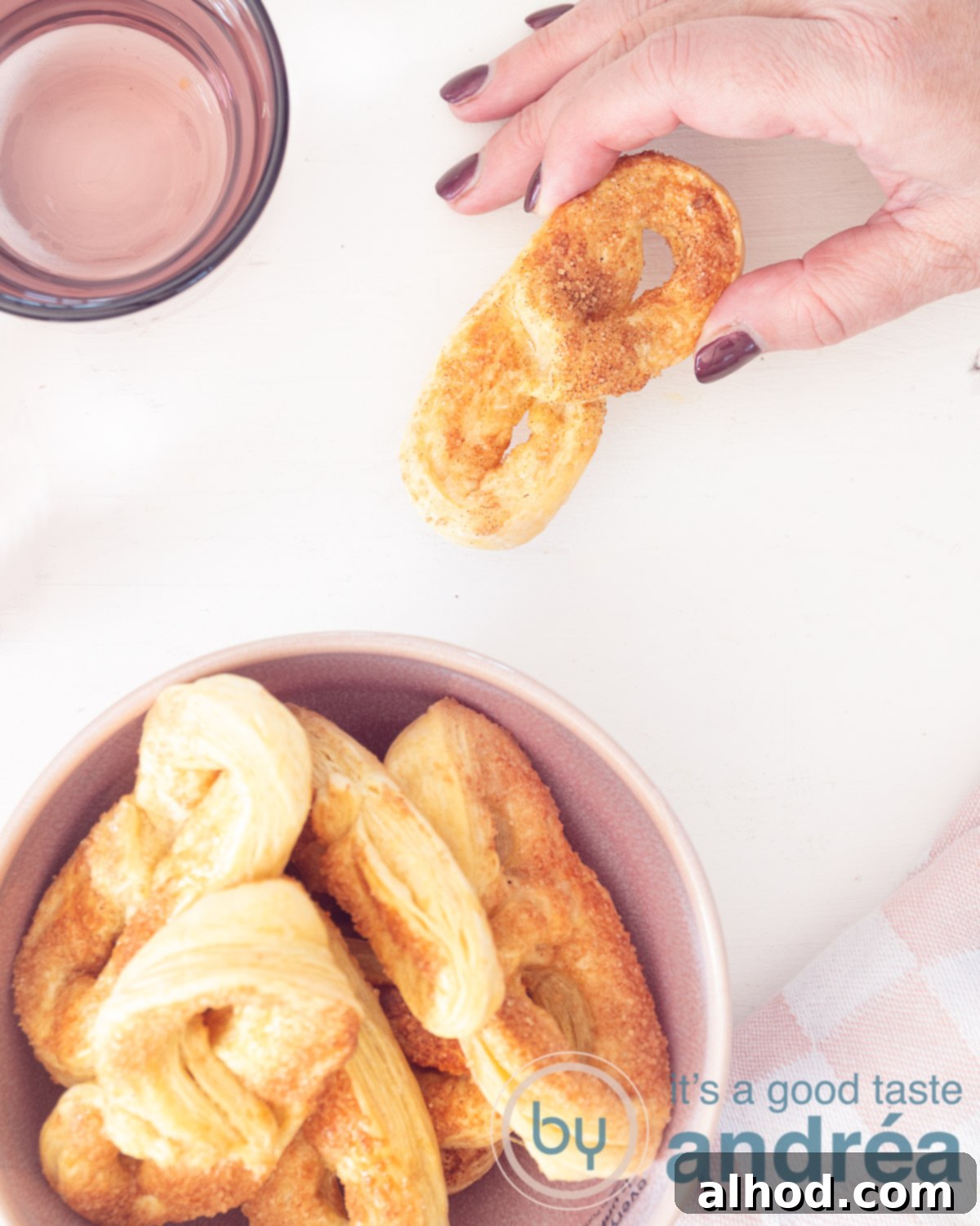 Dutch Krakelingen Sweet Pretzel Cookies 2 Sweet pretzels in a pink bowl. A hand in the upper left corner taking a krakeling. A white background