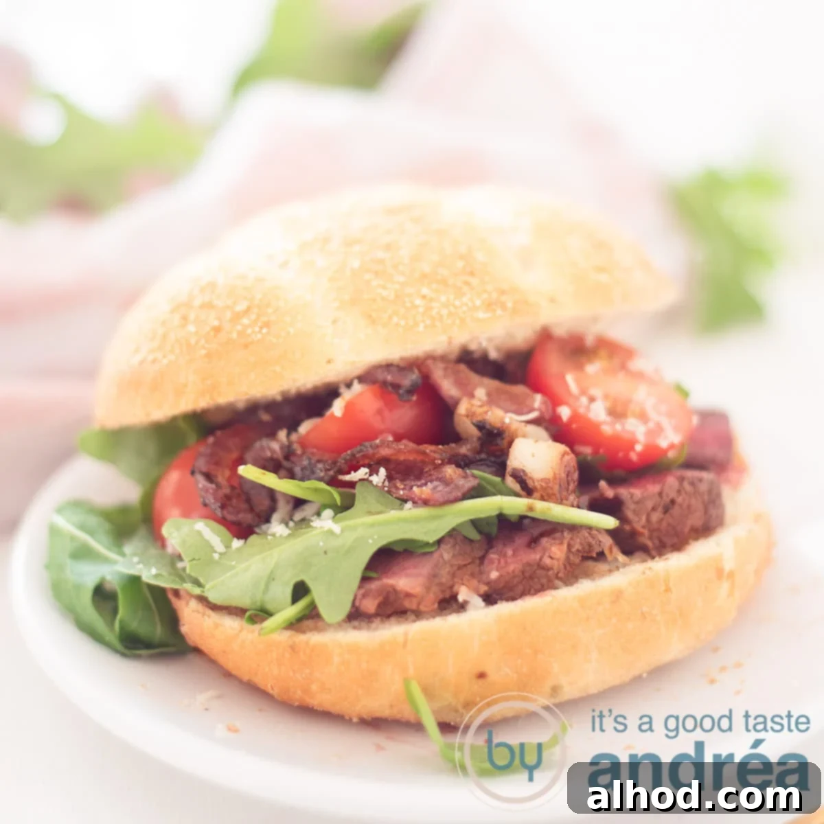Sizzling Steak Sensation 6 A square photo with an Italian bun, filled with slices of steak, caramelized onions, arugula, Parmesan cheese and tomatoes. A pink white cloth and rocket in the background,