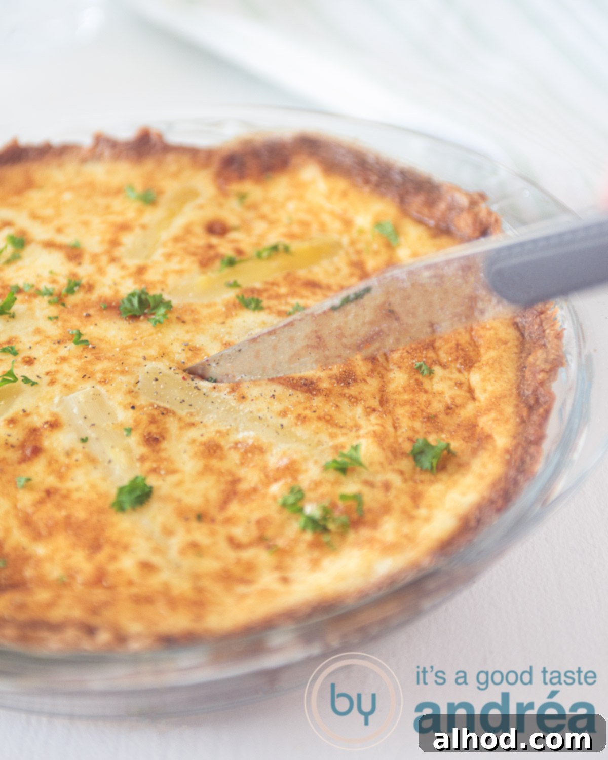Vegetarian White Asparagus Quiche 5 A glass pie dish filled with a savory tart with white asparagus and egg. A knife slicing through. All on a white background