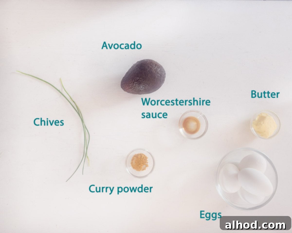 Velvet Avocado Deviled Eggs 3 A beautifully arranged flat lay photo of the ingredients required for Creamy Avocado Deviled Eggs, including eggs, a ripe avocado, butter, curry powder, Worcestershire sauce, and fresh chives, all set on a clean white background with descriptive text.