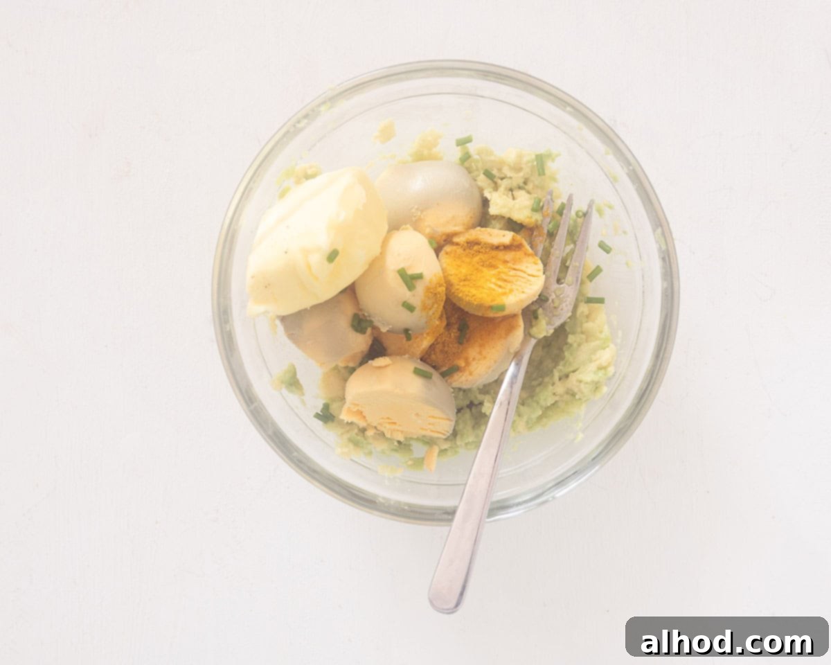 Velvet Avocado Deviled Eggs 5 A glass bowl containing a vibrant green mixture of mashed avocado and bright yellow egg yolks, blended together to create the creamy deviled egg filling.