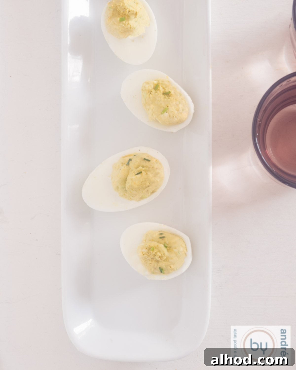 Velvet Avocado Deviled Eggs 8 A high-angle, overhead shot of a white serving plate featuring four beautifully arranged avocado deviled eggs, their creamy green filling topped with fresh chives, ready to be enjoyed.