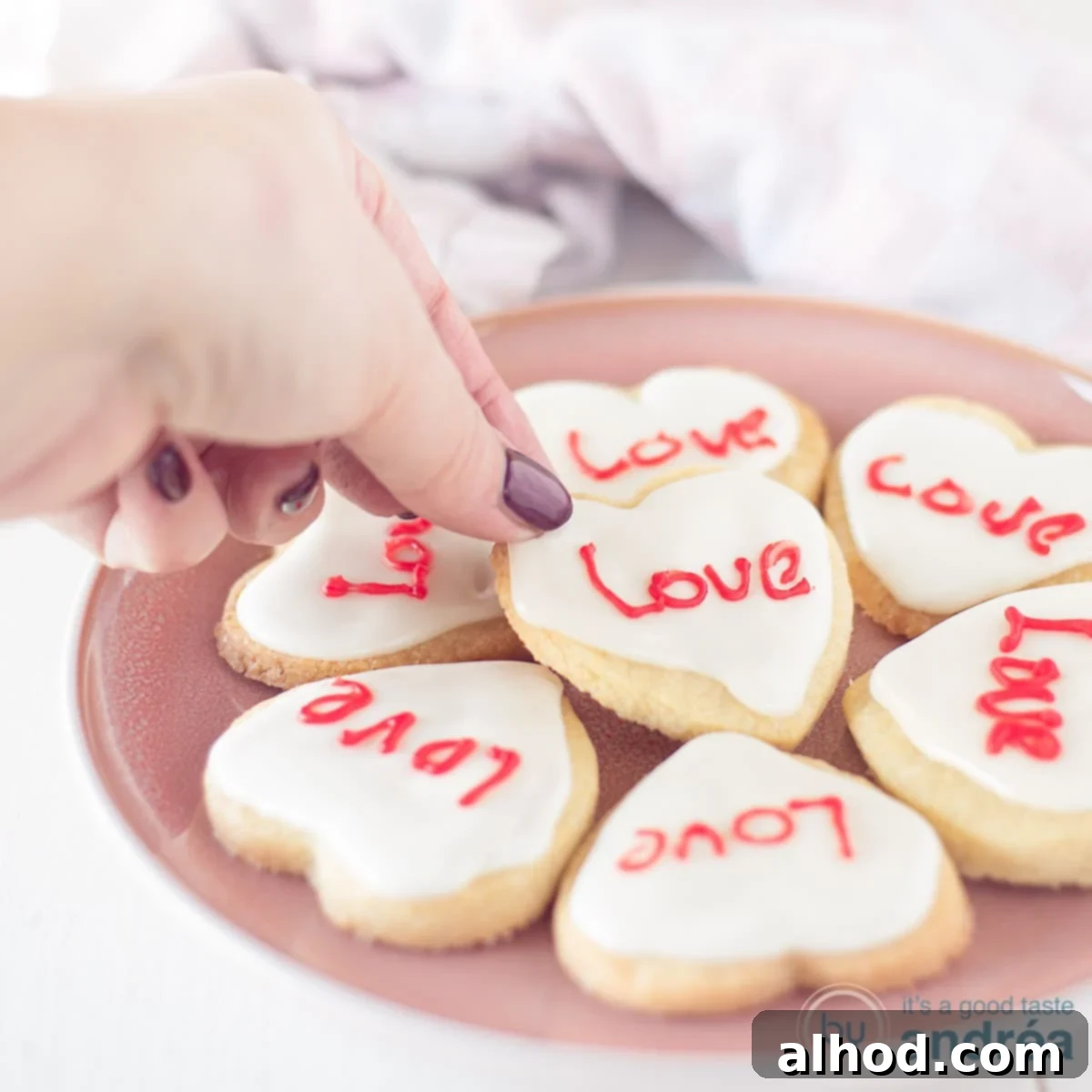 Sweetheart Cookies 4 A square photo with a pink plate with heart cookies with icing and text in red. A hand grabs a cookie.