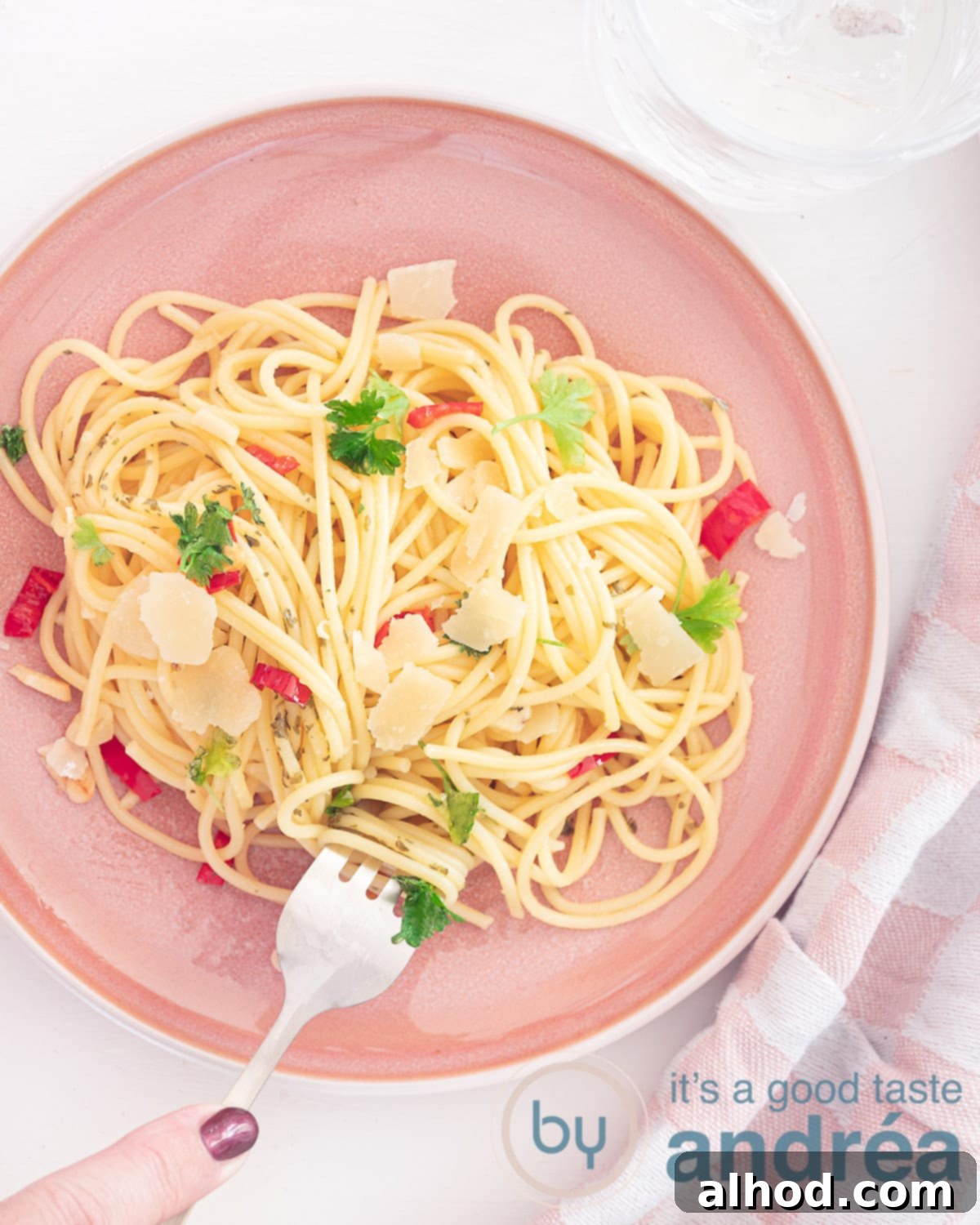 Hot Chili Garlic Pasta 2 A photo from above showing a pink plate of spaghetti, aglio, olio e peperoncino, and fresh parsley. A fork takes a bite of the spaghetti, emphasizing its perfect texture. The dish is set against a clean white background.