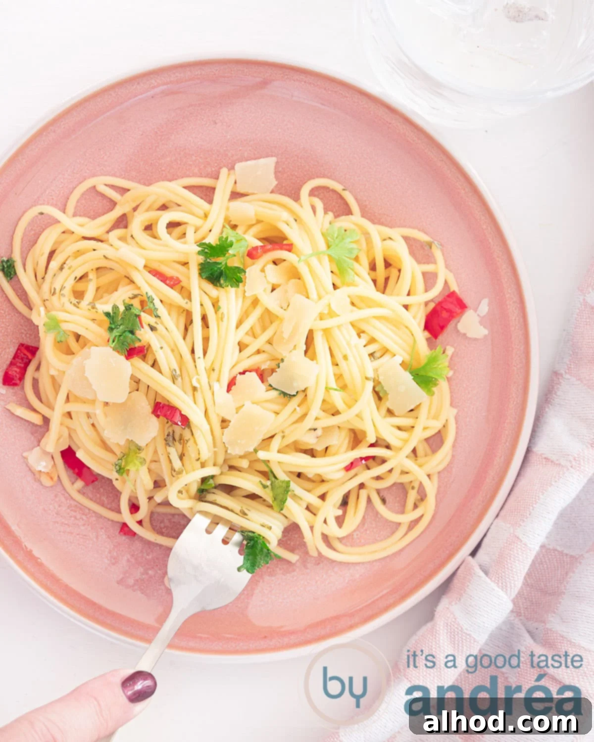 Rustic Chili Garlic Pasta 2 A photo from above showing a pink plate of spaghetti, aglio, olio e peperoncino and parsley. A fork takes a bite of the spaghetti. A white background
