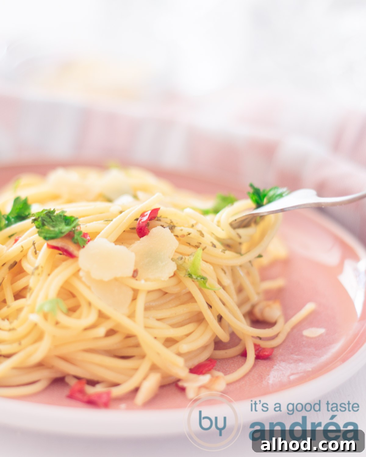 Hot Chili Garlic Pasta 5 A close-up shot of a pink plate filled with a generous portion of spaghetti aglio, olio e peperoncino, garnished with vibrant parsley and grated Parmesan cheese. A fork is poised to take a bite, highlighting the dish's allure.