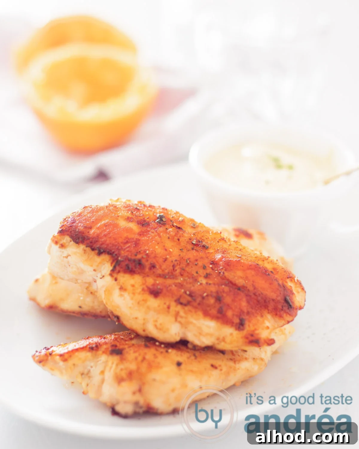 Easy 20-Minute Orange Thyme Skillet Chicken 2 Juicy chicken breast with a delicious orange thyme sauce on a white plate, garnished with fresh thyme sprigs. Some fresh oranges are visible in the background, hinting at the citrusy flavor.