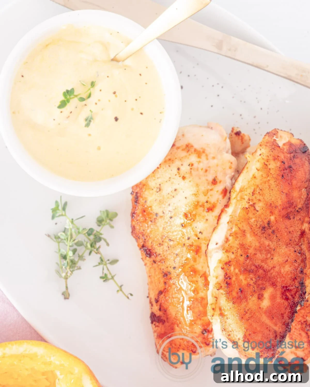 Easy 20-Minute Orange Thyme Skillet Chicken 3 An overhead shot of a rustic white bowl filled with perfectly golden-brown fried chicken breasts. To the top left, a small bowl holds the creamy orange thyme sauce, with loose sprigs of fresh thyme scattered around, enhancing the natural and aromatic appeal of the dish.