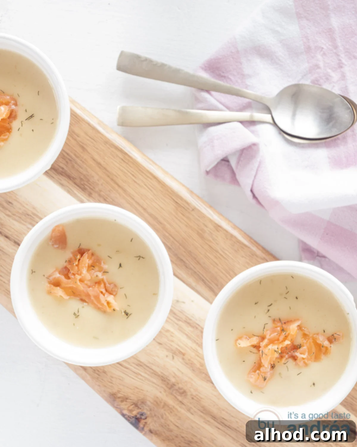 Regal Dutch Broth 4 Three elegant bowls filled with Koninginnensoep, a creamy chicken soup, garnished generously with vibrant smoked salmon and fresh dill, arranged on a rustic wooden board, ready to be served.