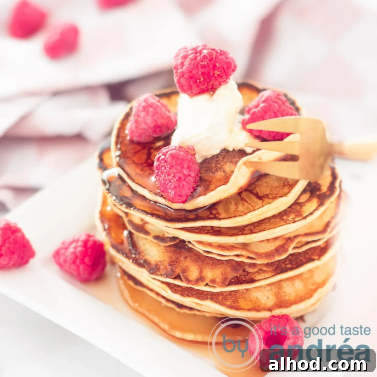 Decadent Raspberry Crème Fraîche Pancakes 5 A square photo showcasing a towering stack of golden American pancakes, generously topped with an inviting swirl of crème fraîche and a colorful scattering of fresh red raspberries. A charming pink and white striped cloth is visible in the soft-focus background, enhancing the cozy appeal of this delicious breakfast or brunch.
