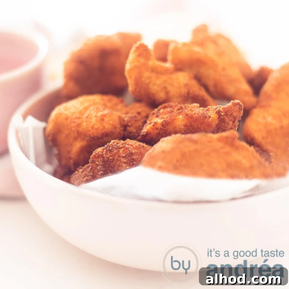 Parmesan Crusted Chicken Nuggets 6 A square photo with a pink bowl filled with golden Parmesan Chicken Nuggets on a white background.