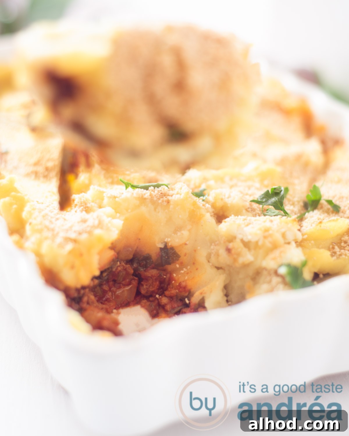 Comforting Beef, Potato and Spinach Bake 2 A beautifully golden-brown Potato and Ground Beef Casserole with Spinach in a white oven dish, with a scoop removed revealing the savory layers beneath. A serving spoon rests in the dish.