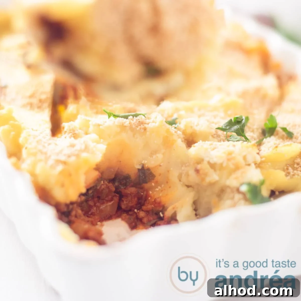 Comforting Beef, Potato and Spinach Bake 4 A close-up, square photo of a white baking dish showcasing a generous portion of spinach, ground beef, and fluffy mashed potatoes, ready to be served.