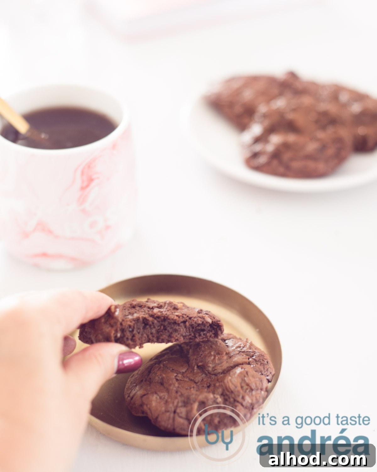 Fudgy Brownie Walnut Cookies 5 Brownie Walnut Biscuits on a golden platter. A hand takes it off. In the left background a pink mug with coffee. A sign with more brookies in the back right. A white background.