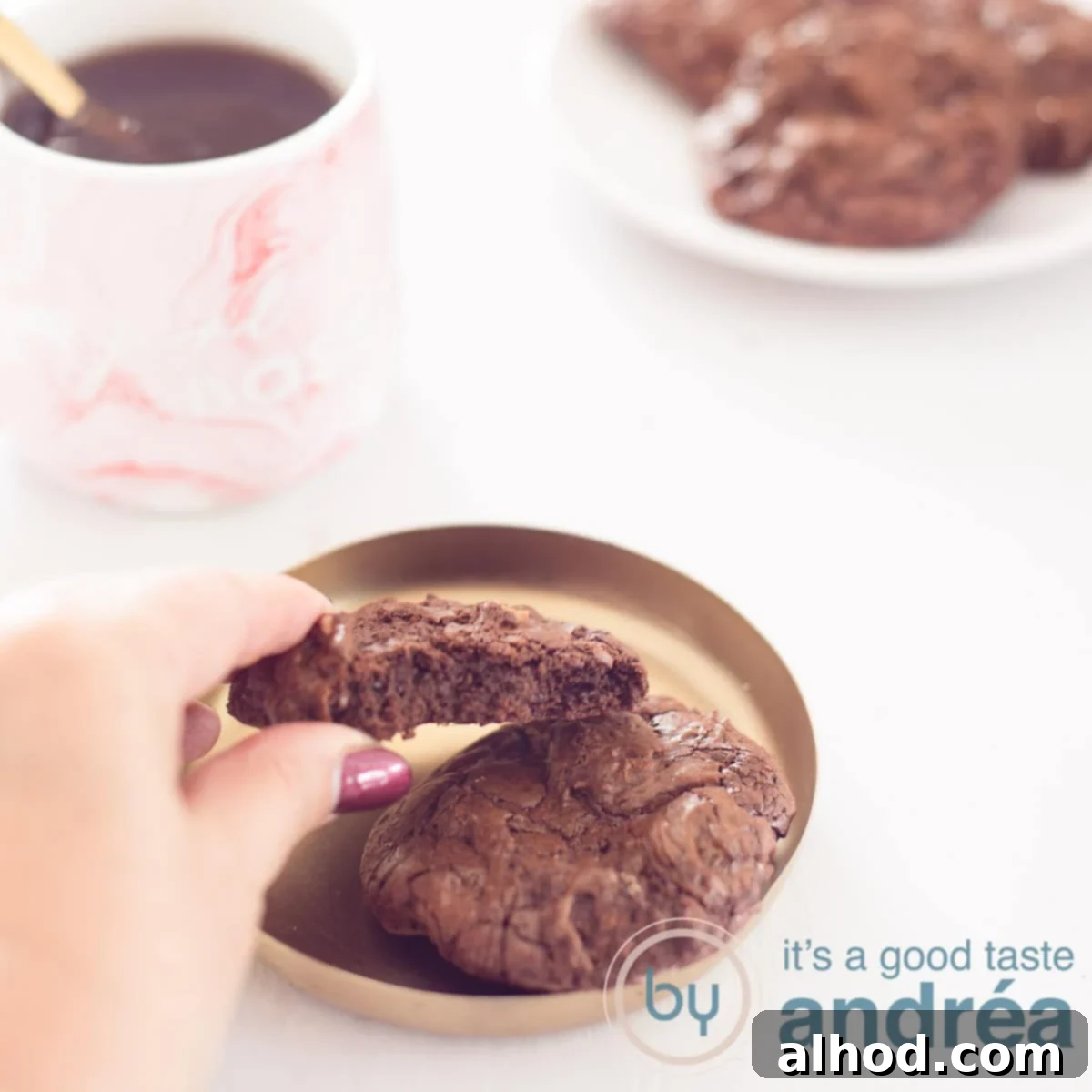 Fudgy Brownie Walnut Cookies 6 A square photo with a Brownie cookie, a hand takes it off the tray. In the back left is a pink mug with coffee. At the top right a white board with a number of brookies. A white background